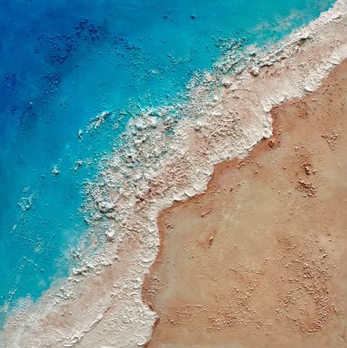 Vista aérea de la costa, con agua azul y arena beige.